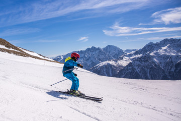 Little boy in blue and yellow ski costume skiing in downhill slope. Winter sport recreational activity