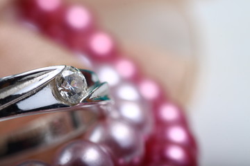 Close up shoot of an engagement ring on a pink pearl bracelet
