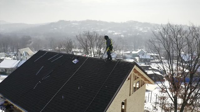 Aerial zooming out view of smiling tiler standing on the roof top of residential house under constuction. Bright blue sky is on the background