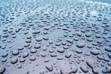 Extreme macro close-up of clean car paint surface with multiple water drops after heavy rain and dew water repellent surface treatment blue color tones