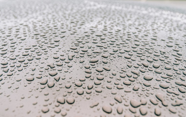 Extreme macro close-up of clean car paint surface with multiple water drops after heavy rain and dew water repellent surface treatment warm color tones