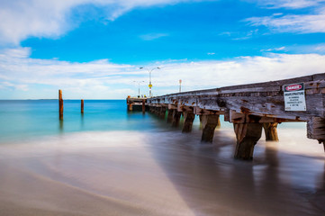 Obraz premium Long exposure, blue sky, moving water, beach, fishermen on jetty 