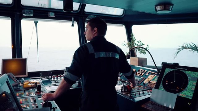 Marine navigational officer during navigational watch on Bridge . He is maneuvering the ship. Work at sea.