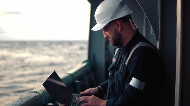 Marine chief officer or captain on deck of vessel or ship watching laptop. Internet and home connection at sea.