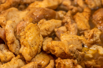 Marinated torn cut chicken bits being cooked, halfway cooked. Spicy chicken, wooden spatula