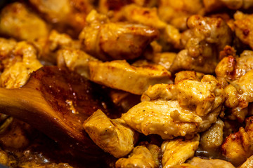 Marinated torn cut chicken bits being cooked, halfway cooked. Spicy chicken, wooden spatula