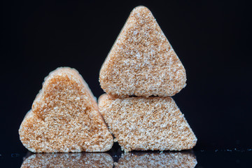 A piece of refined sugar with cinnamon on a black background. Photographed close-up.