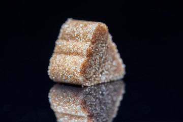 A piece of refined sugar with cinnamon on a black background. Photographed close-up.