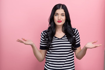 Young woman shrugging on a pink background