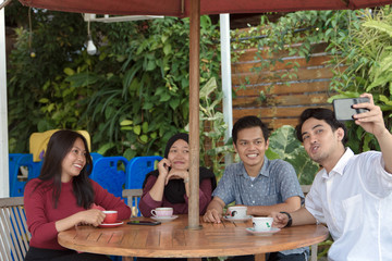 Multiracial group of four asian friends having a coffee together. Two women and two men at cafe, talking, laughing and enjoying their time