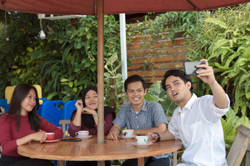 Multiracial group of four asian friends having a coffee together. Two women and two men at cafe, talking, laughing and enjoying their time