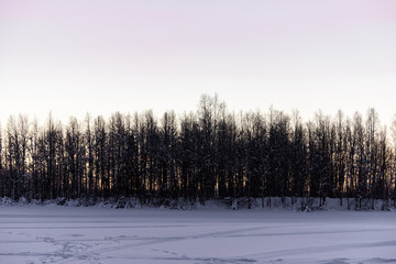 The ice lake and forest has covered with heavy snow and sunset sky in winter season at Holiday Village Kuukiuru, Finland.