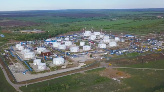 Aerial view large white round reservoirs with blue pipelines among green lawns at gas and oil refinery plant. Clip. Transneft, tanks and oil extraction factory with storage at summer sunny day.