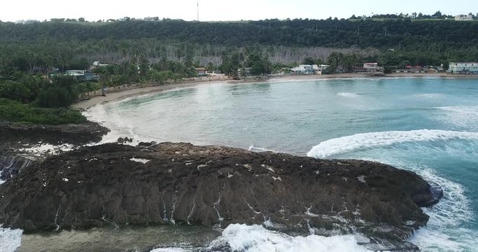 Aerial shot of beach rock and waves crashing in Jobos Puerto Rico with town in background