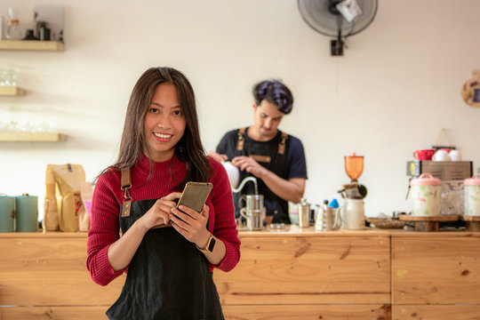 Portrait of a smiling young Asian female entrepreneur standing with her smartphone or cellphone