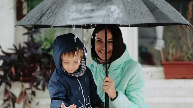 Young mother with her son hide under an umbrella during the rain