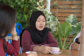 Asian muslim woman with head scarf enjoying coffee or tea with his girlfriend sitting in an outdoors cafe.