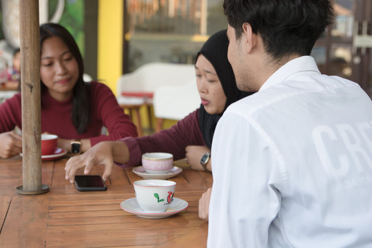 Multiracial group of four asian friends having a coffee together. Two women and two men at cafe, talking, laughing and enjoying their time