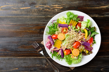 Healthy vegetables salad and fork on wooden background, top view