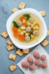 Soup with meatballs served in a white plate over grey concrete background, flatlay, studio shot