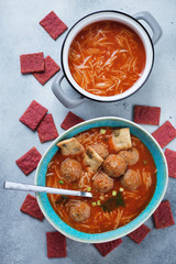 Tomato soup with meatballs and vermicelli, above view over light-blue stone background, vertical shot