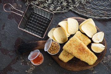 Rustic wooden serving board with fish and chips snack, above view over browne stone background,...