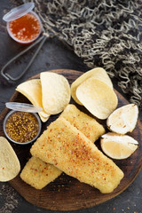 Top view of breaded fish fillet with potato chips and dips, closeup on a brown stone surface with a fishing net