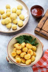 Roasted and uncooked italian potato gnocchi, vertical shot over beige stone background