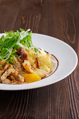 Closeup view of salad with fried chicken meat, dried tomato, cashew nuts and orange balsamic sauce served with arugula and parmesan on dark wooden background
