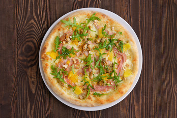 Pizza with turkey, bacon, orange and cashew nuts on dark wooden background