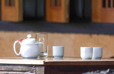 White jug and mug of tea on a wooden table Background Blurry wooden windows.