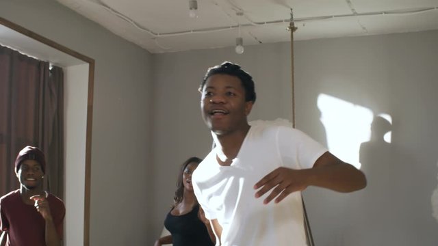 Handheld tracking of cheerful black men and woman smiling and dancing afro house style in studio