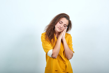 Sleepy young woman in yellow jacket keeping hand on head, sleeping gesture isolated on gray...