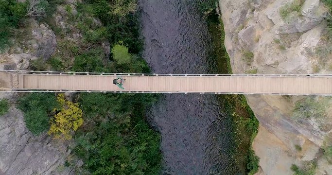 vuelo ascendente de dron y vista cenital de puente colgante y caminante senior