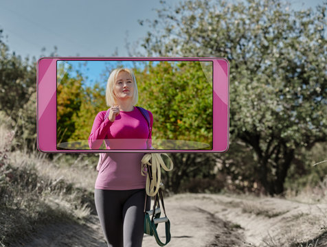 Young smiling woman with suspension straps going to training in park, smart device concept