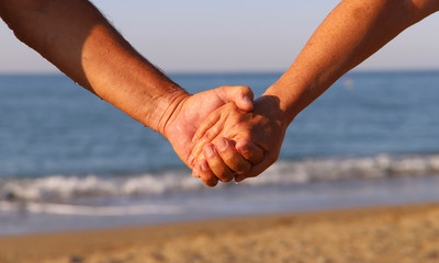 Hands of man and woman against the background of the sea. The joined hands of man and woman. The concept of love and family.