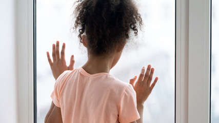 Upset little girl look in window feeling lonely