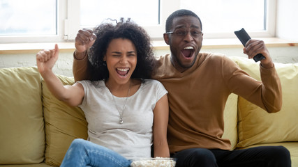 Excited biracial couple have fun watching sports game together
