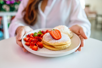 A woman holding and showing a plate of pancakes with strawberries and whipped cream