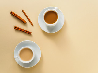 Coffee in white cups and cinnamon sticks on a yellow background. Space for text