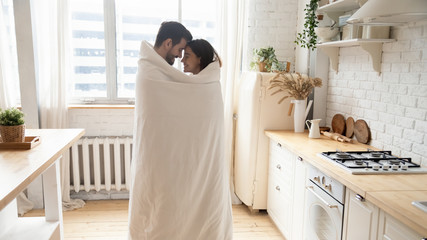 Young affectionate couple standing in kitchen wrapped with blanket