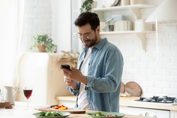Happy young man preparing romantic dinner using smartphone app