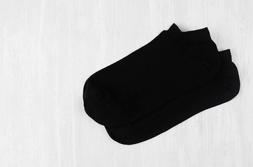 Pair blank black small, low socks flat lay on white wood board, side view - mock up for design, print, presentation, advertising, top view, copy space.