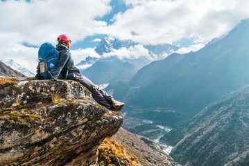 Young hiker backpacker female sitting on the cliff edge and enjoying Ama Dablam 6,812m peak view...