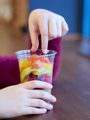 children's hands hold glass with exotic fruits: mango, kiwi, strawberry, pineapple, pitaya, cactus fruit.  wooden table. health organic food. Exotic. close up. Salad