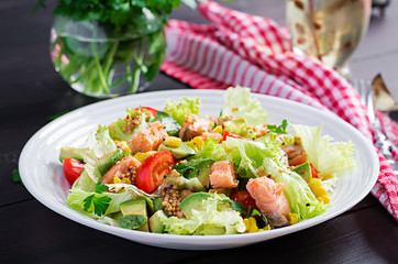 Salad with grilled salmon, lettuce, avocado, tomatoes and corn on a white bowl. Paleo diet.