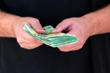 Mann in schwarzem Shirt überreicht ein Bündel grüne 100-Euro Scheine
