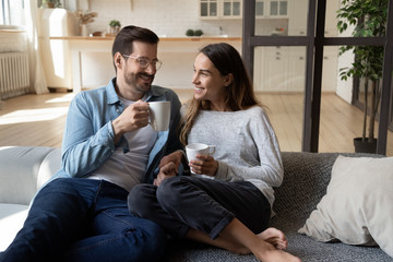 Happy young couple relaxing on sofa talking drinking tea