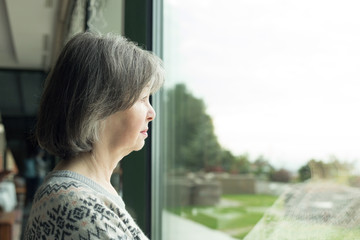 Lonely senior woman looking through window