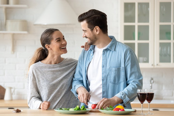 Cheerful young couple cutting salad cooking together in kitchen interior
